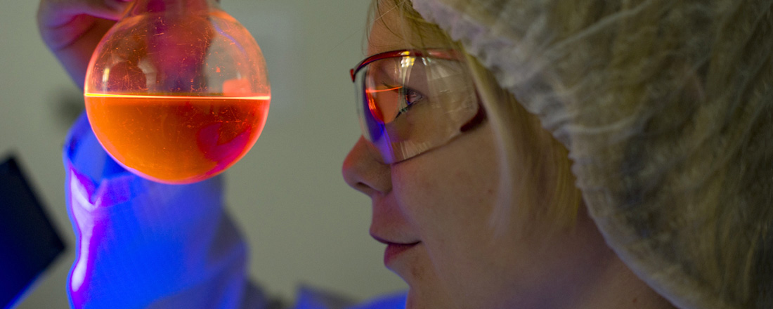Frau schaut auf ein mit orangener Flüssigkeit gefülltes Reagenzglas